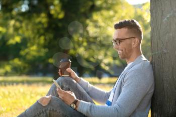 Handsome man with mobile phone and cup of coffee resting in park�