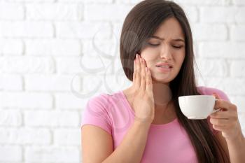 Young woman with sensitive teeth and cup of hot coffee on blurred  background�