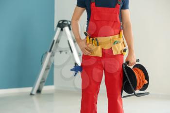 Electrician with extension cord reel and tools in new empty apartment�