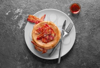 Plate with tasty pancakes and bacon on grey table�