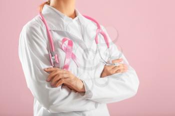 Doctor with pink ribbon on coat against color background, closeup. Breast cancer awareness concept�