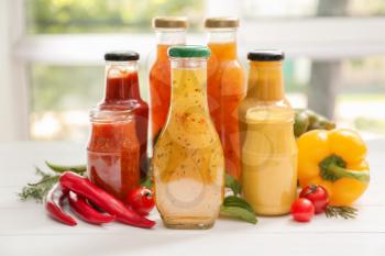 Glassware with different tasty sauces and vegetables on white table�