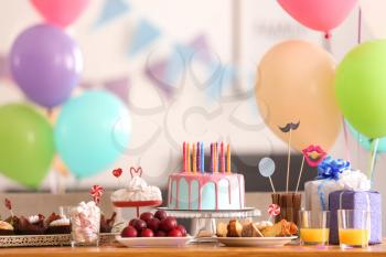 Beautiful birthday cake with candles and different sweets on table�