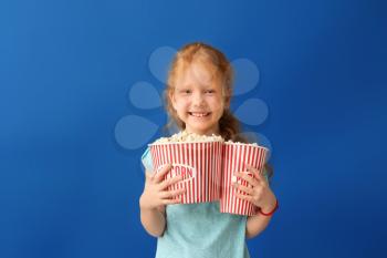 Cute little girl with cups of popcorn on color background�