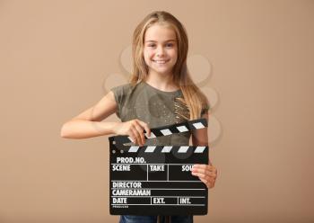 Cute little girl with clapper board on color background�
