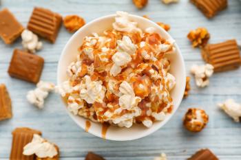 Bowl full of delicious popcorn with caramel on wooden background, top view�