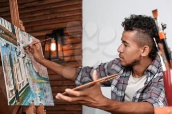 Young African-American artist painting picture in workshop�