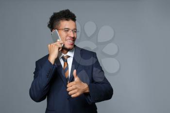 Handsome African-American businessman talking by mobile phone on grey background�