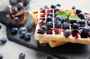 Delicious waffles with blueberries and jam on slate plate, closeup�