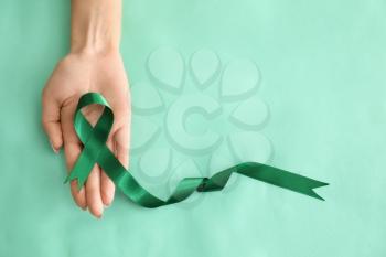 Woman holding green ribbon on color background. Kidneys cancer awareness concept�
