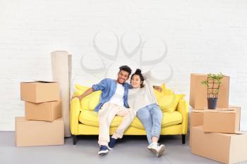 Happy interracial couple resting on sofa near carton boxes in room. Moving into new house�