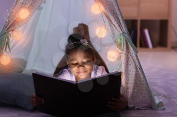 Little African-American girl reading bedtime story in hovel�
