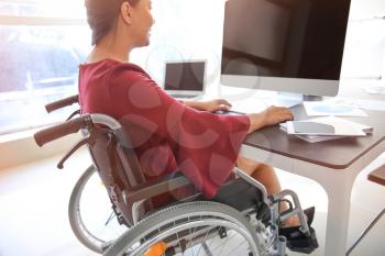 Asian woman in wheelchair working with computer in office�