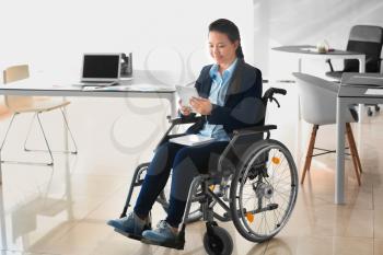 Asian woman in wheelchair working with tablet PC in office�