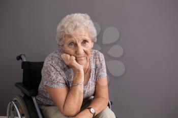 Upset senior woman in wheelchair on grey background�