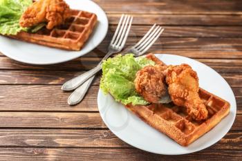 Plates with delicious waffles and chicken on wooden table�