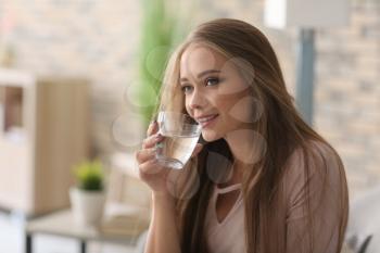 Beautiful young woman drinking water at home�