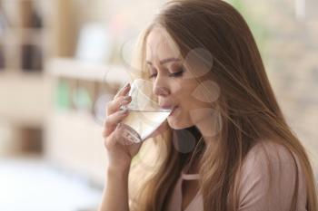 Beautiful young woman drinking water at home�