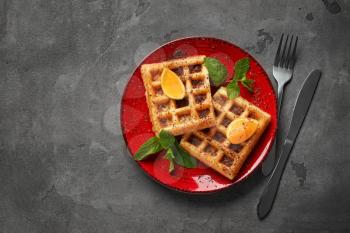 Tasty waffles with cut orange on plate�