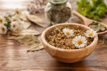Bowl with dried chamomile flowers on wooden table�