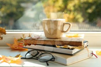 Cup of hot coffee with books and autumn leaves on windowsill�