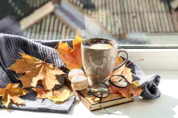 Cup of aromatic tea with book, warm sweater and autumn leaves on windowsill�