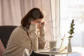 Depressed young woman using laptop at home�