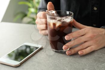 Woman with glass cup of cold coffee and mobile phone at grey table�