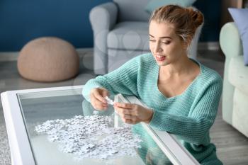 Woman assembling puzzle on glass table at home�