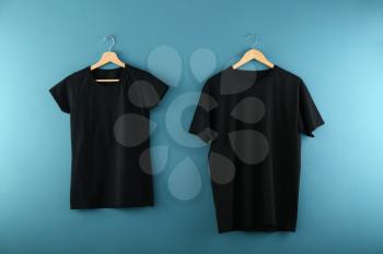 Hangers with blank black t-shirts on color background�