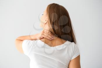 Young woman suffering from neck pain on light background�