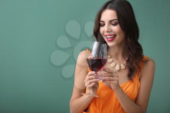 Beautiful young woman with glass of wine on color background�