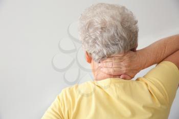 Senior woman suffering from neck pain on light background�