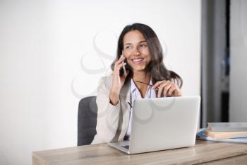 Young woman with laptop talking by mobile phone in office�