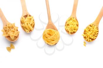 Wooden spoons with various uncooked pasta on white background�
