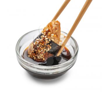 Dipping of tasty sushi into bowl with sauce on white background�