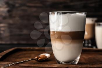 Glass of tasty aromatic latte on wooden board�