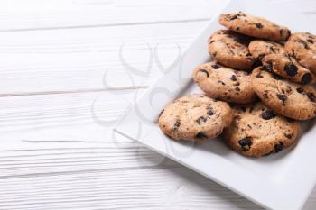 Tasty cookies with chocolate chips on white wooden table�