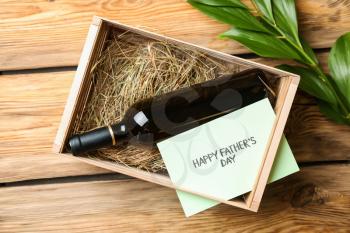 Bottle of wine in box with greeting card for Father's Day on wooden background�
