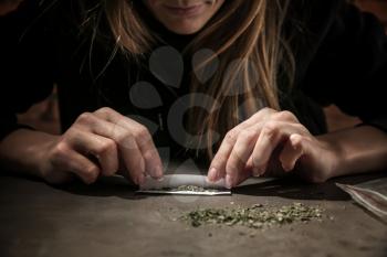 Female junkie making cigarette with marijuana at grey table. Concept of addiction�