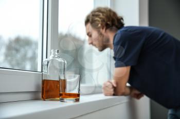 Bottle and glass of whiskey on windowsill in flat of depressed young man. Alcoholism concept�