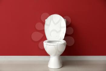 Modern ceramic toilet bowl near color wall in restroom�