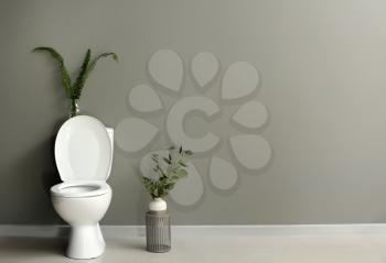 Modern ceramic toilet bowl near grey wall in restroom�