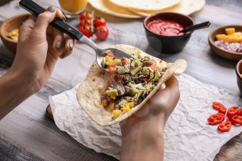 Woman preparing tasty taco on wooden table�