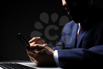 Professional hacker with laptop and mobile phone sitting at table on dark background�