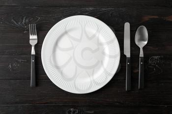 Empty ceramic plate with cutlery on dark wooden background�