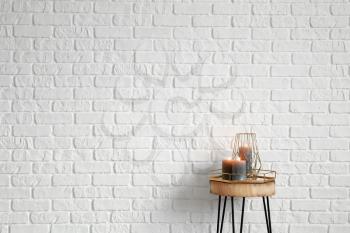 Burning candles on wooden table near white brick wall�