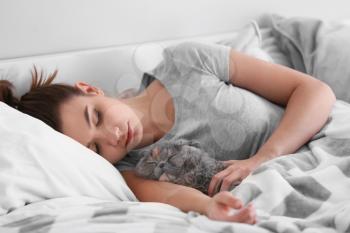 Young woman with cute cat sleeping in bed�