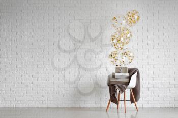 Chair with gifts and balloons near white brick wall�