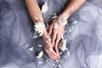 Female hands with white flowers on grey cloth�